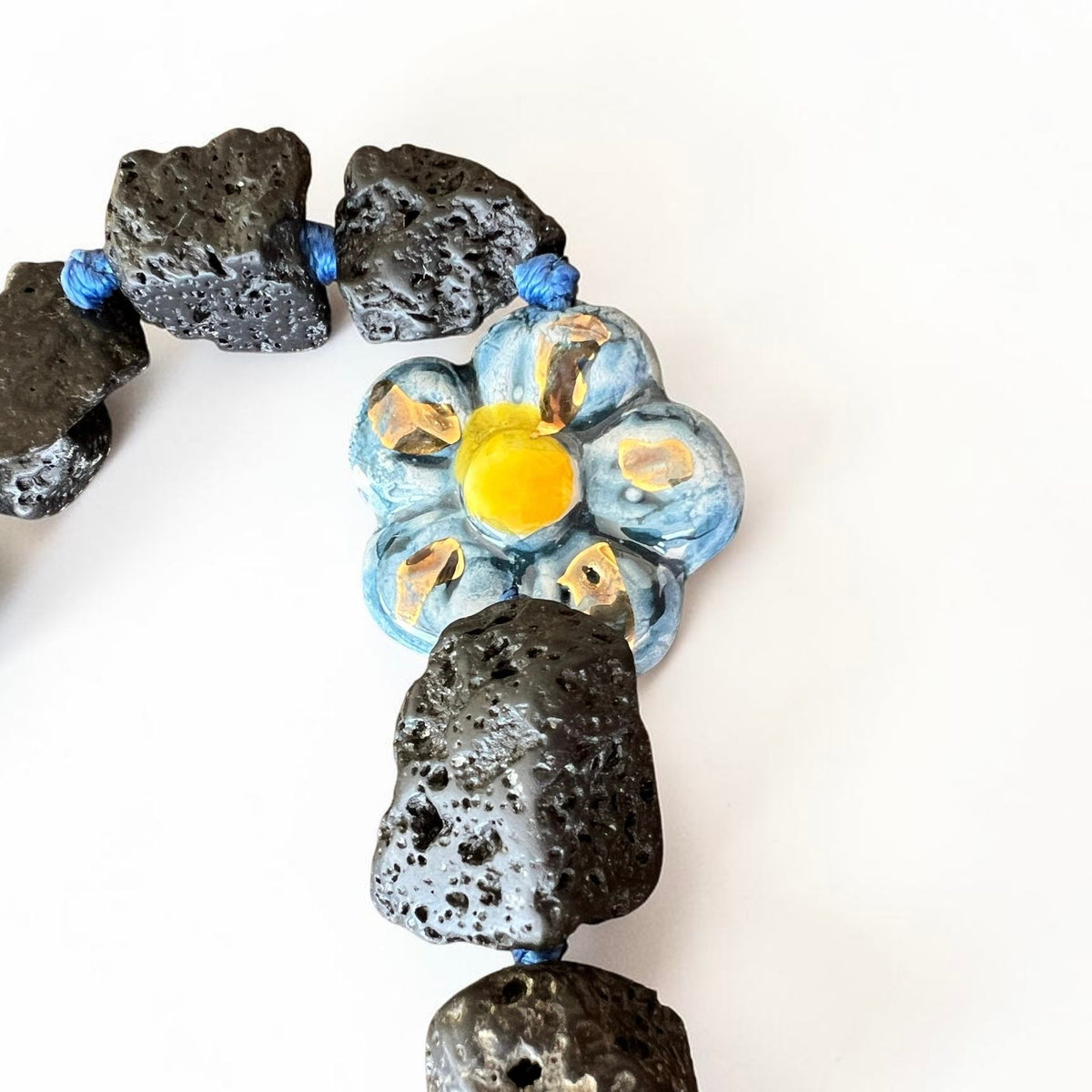 Blue hand-painted Caltagirone ceramic flower surrounded by natural Etna lava stones on Sicilian handmade jewelry