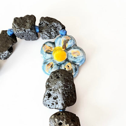 Blue hand-painted Caltagirone ceramic flower surrounded by natural Etna lava stones on Sicilian handmade jewelry
