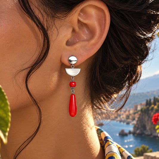 Coral Eclipse drop earring worn by a woman, featuring silver-tone geometric details and a red teardrop pendant.